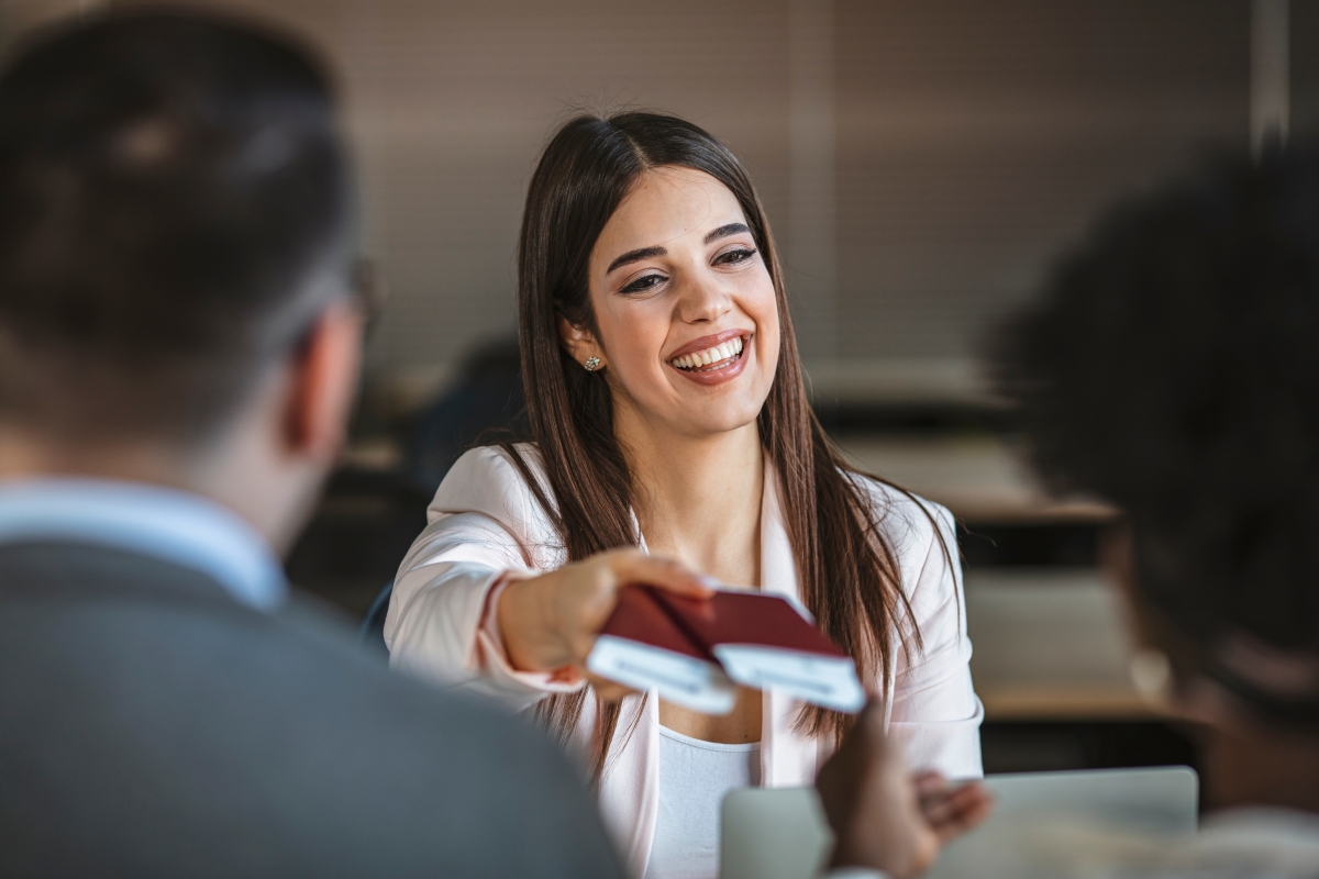 young woman smiling while handing passports and tickets to two people