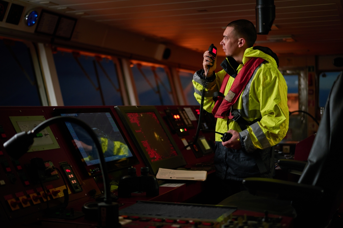 man in safety jacket standing at a desk speaking into a communications device