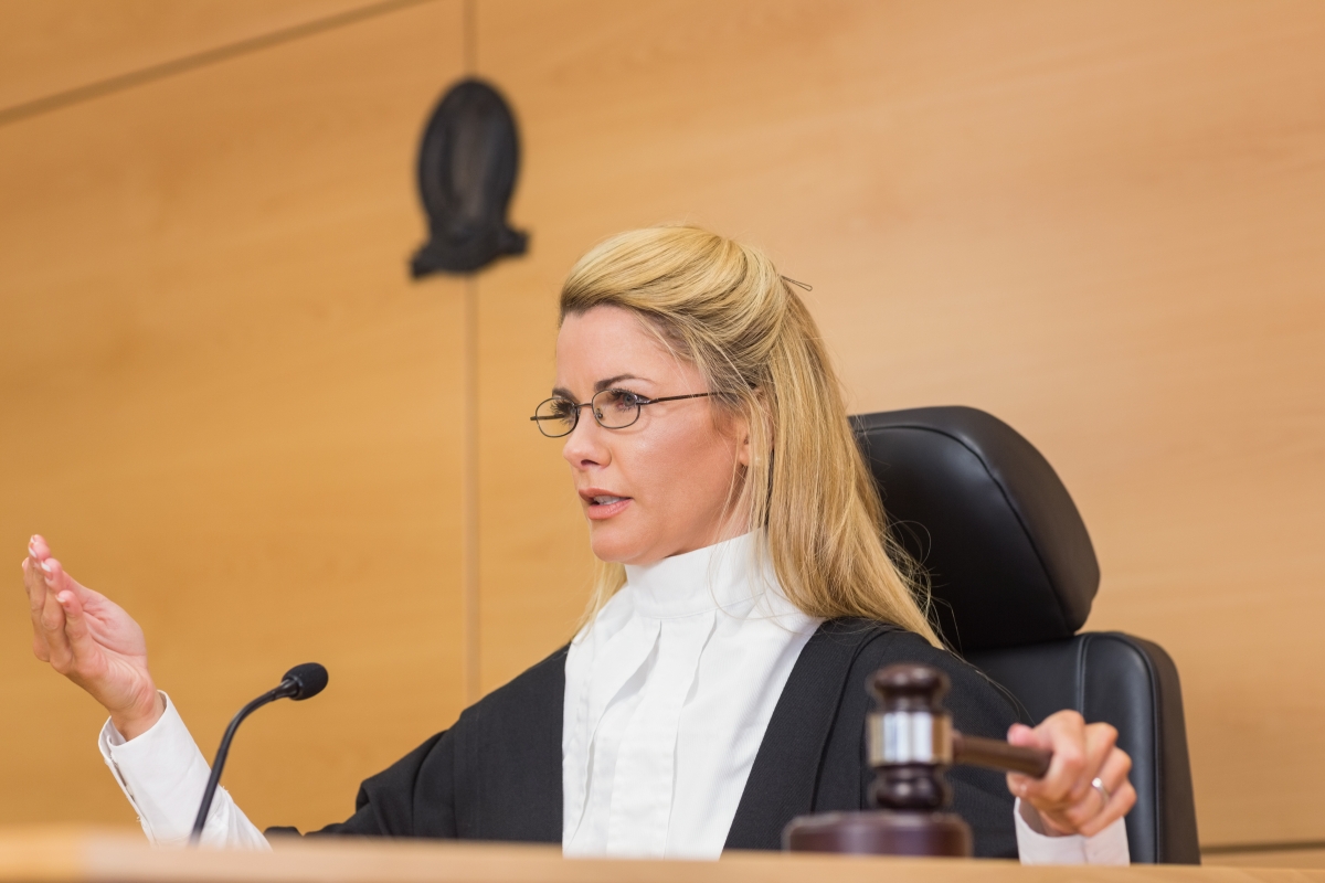 a judge using a gavel and speaking into a microphone while seated at court
