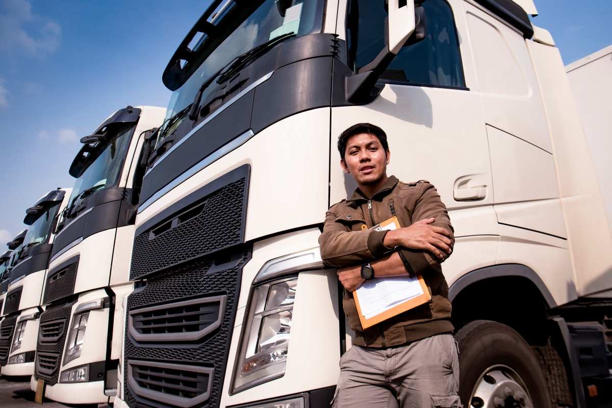 man holding a clipboard and leaning on a large transport truck