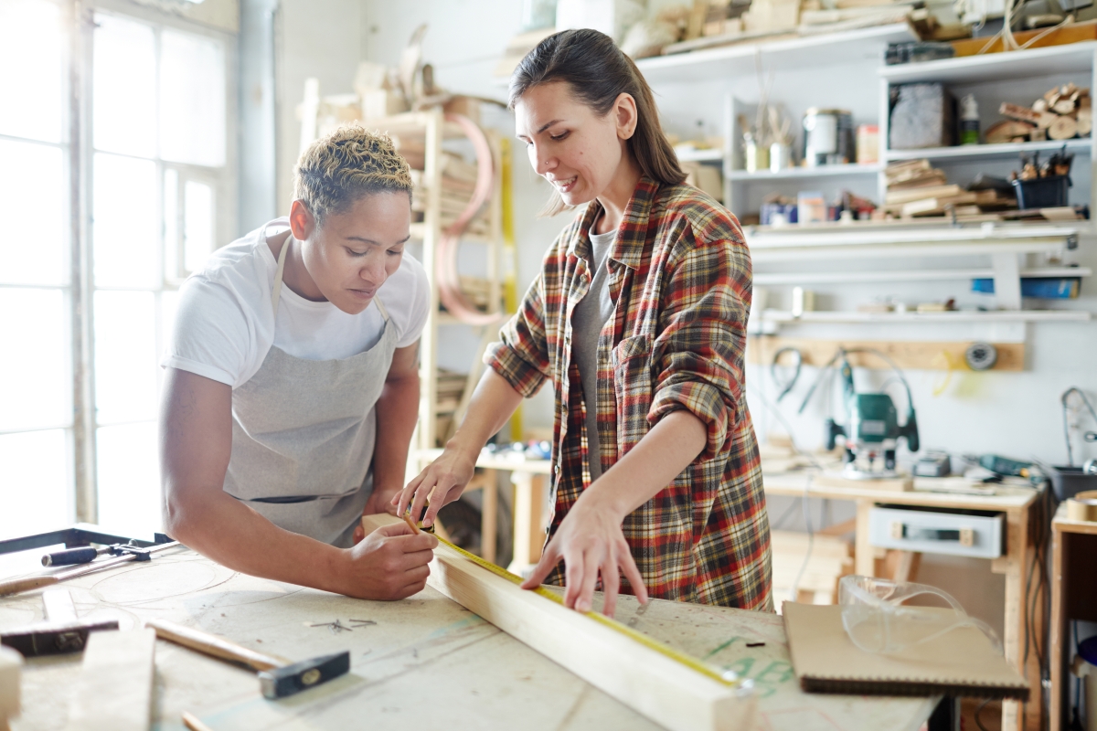two people measuring wood in a workshop