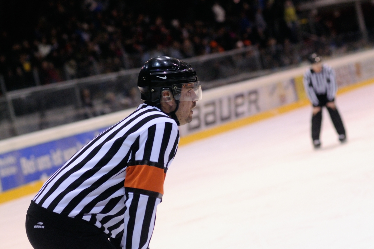 two ice hockey referees skating in an arena while the stadium is filled with spectators in the background