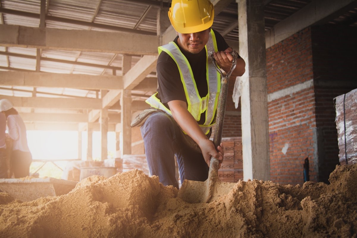 person wearing hard hat and safety vest digging with a shovel at a construction site