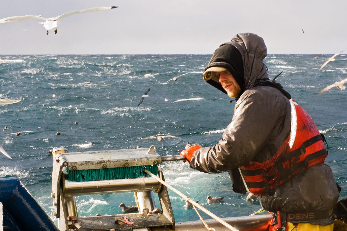 person wearing a life vest, reeling in a net on a fishing boat