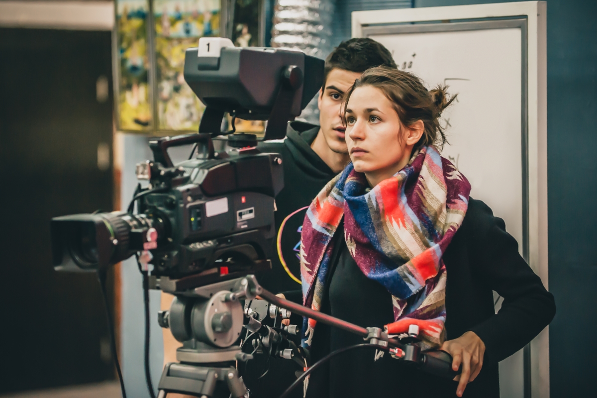 young woman operating a professional video camera as a young man looks on over her shoulder