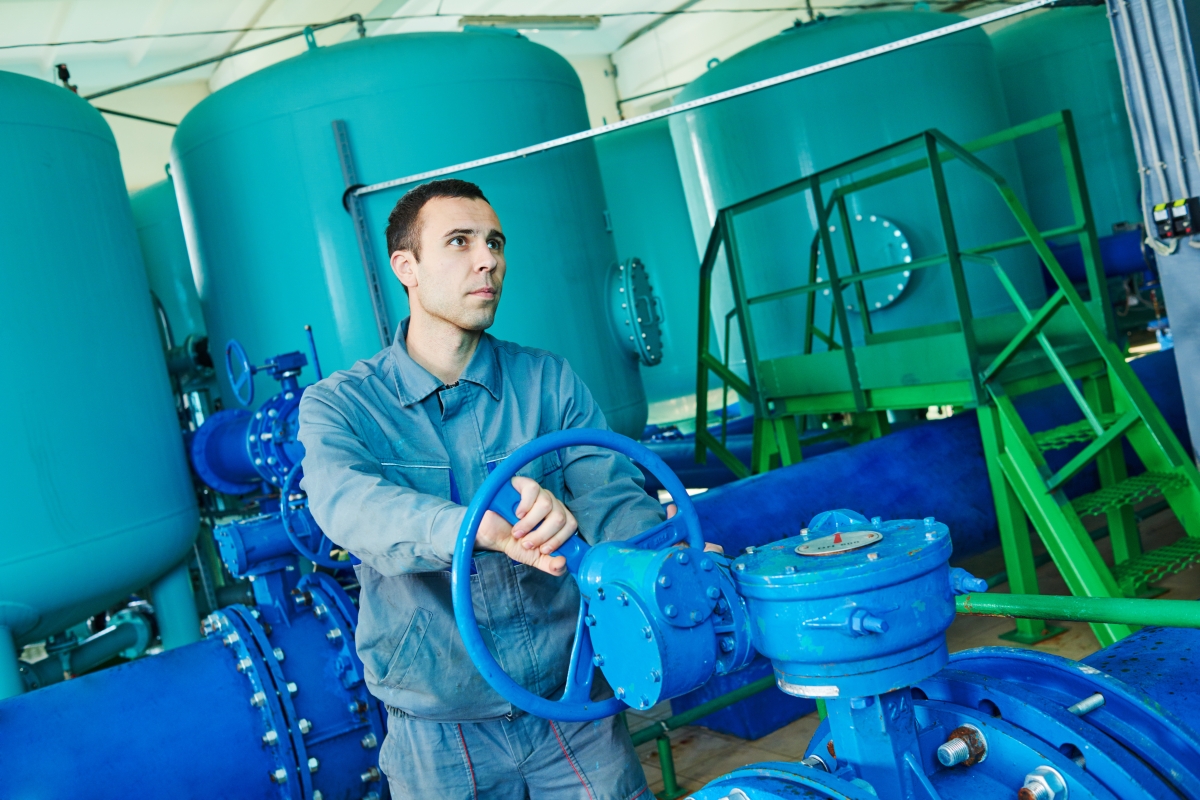 person turning a valve wheel in an industrial plant