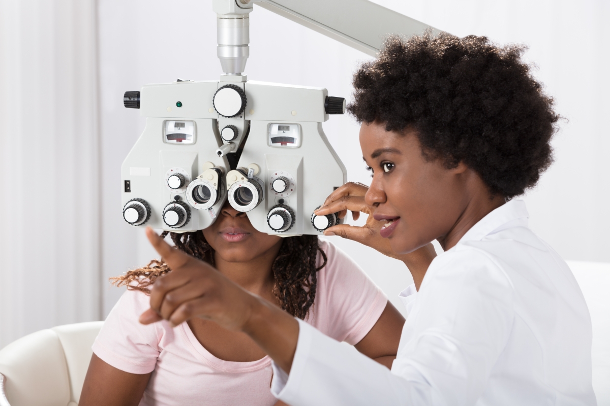 woman wearing a white lab coat using a phoropter to test a patient's eyes