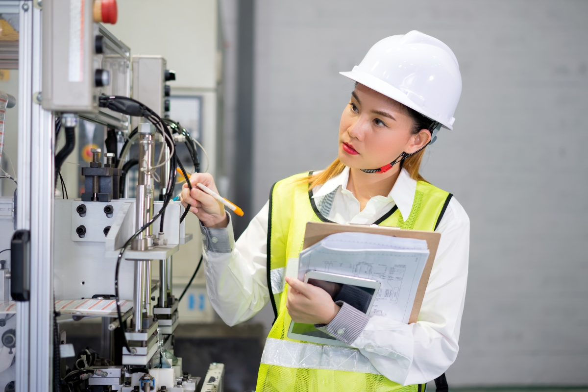person, wearing a hard hat and safety vest, inspecting electrical equipment
