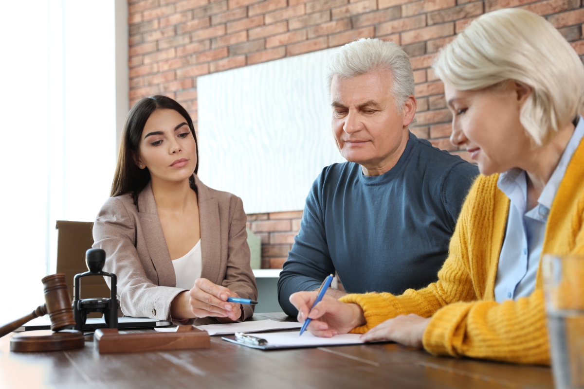 young woman in professional attire seated at a table with an older couple signing paperwork