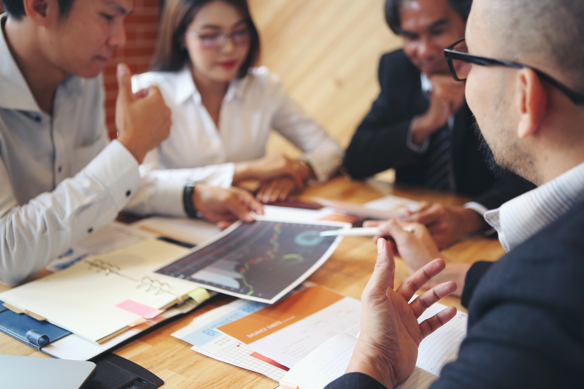 a group of four diverse people sitting around a table looking at documents and talking