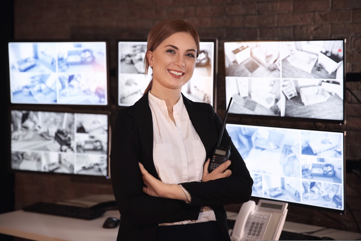 woman holding a handheld radio standing in front of security monitors