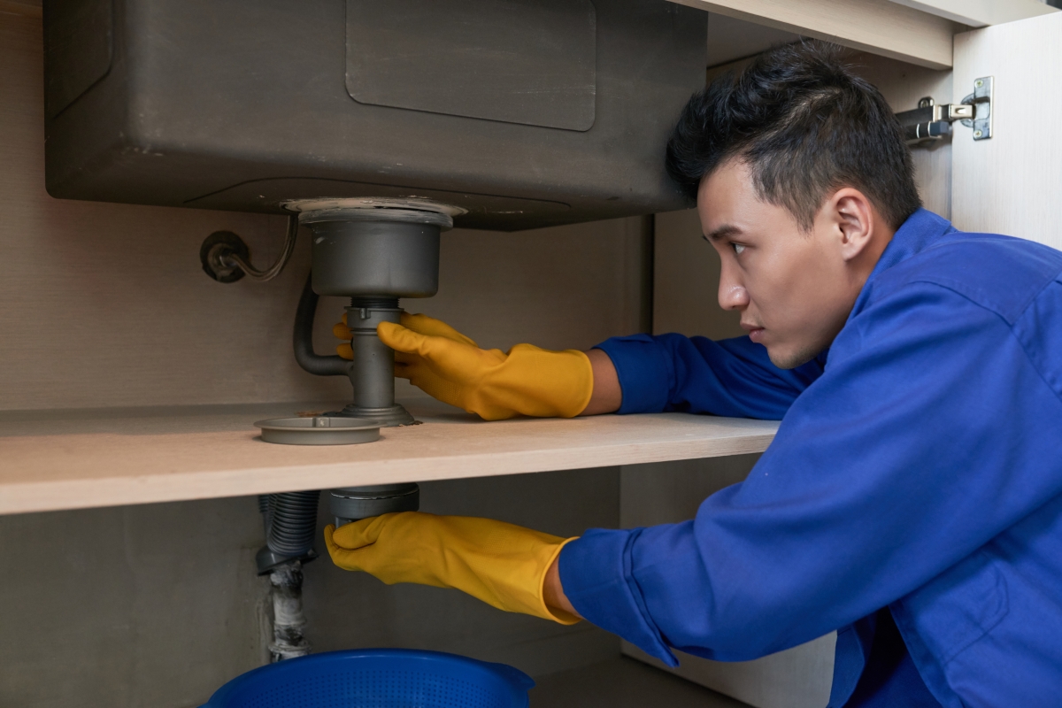 male plumber working on pipes under a sink