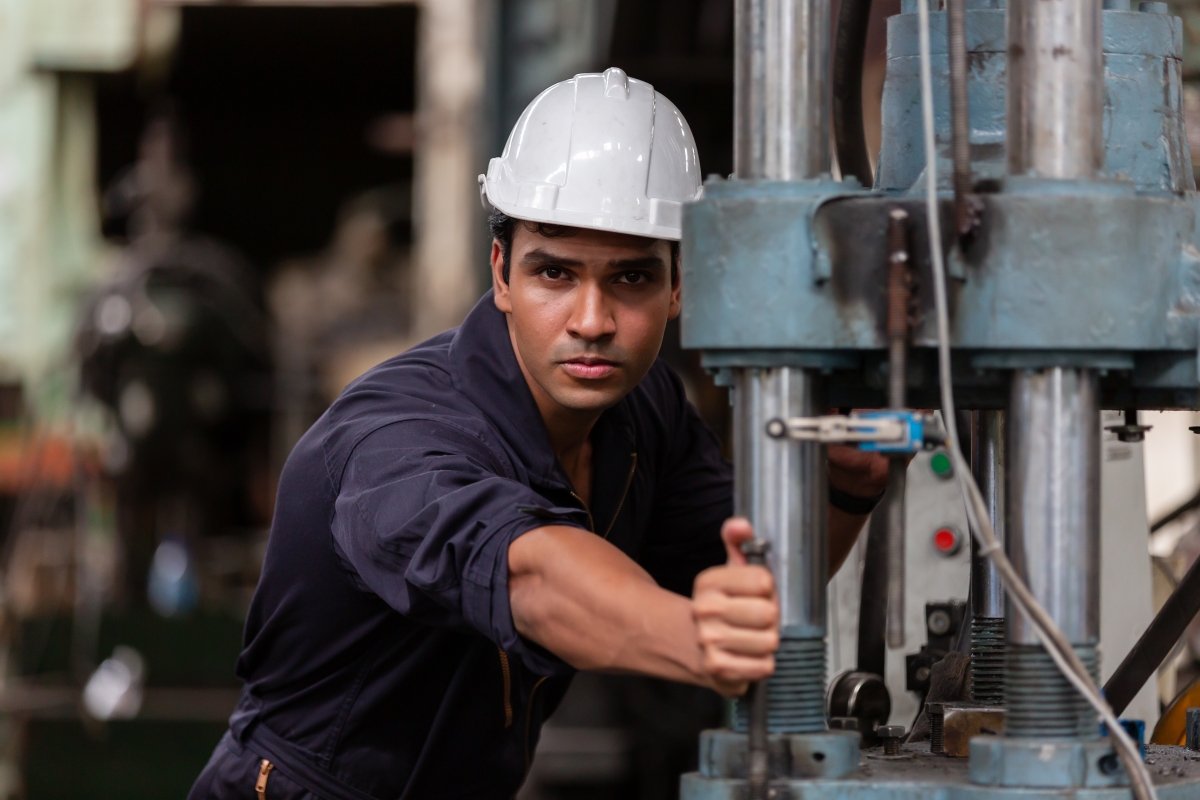 person, wearing a hard hat, working on a piece of industrial equipment