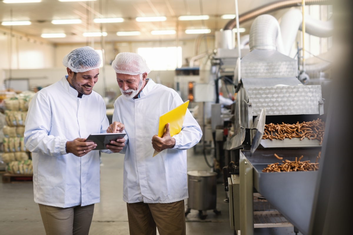 two people, wearing hair nets, looking at a tablet in a food processing plant