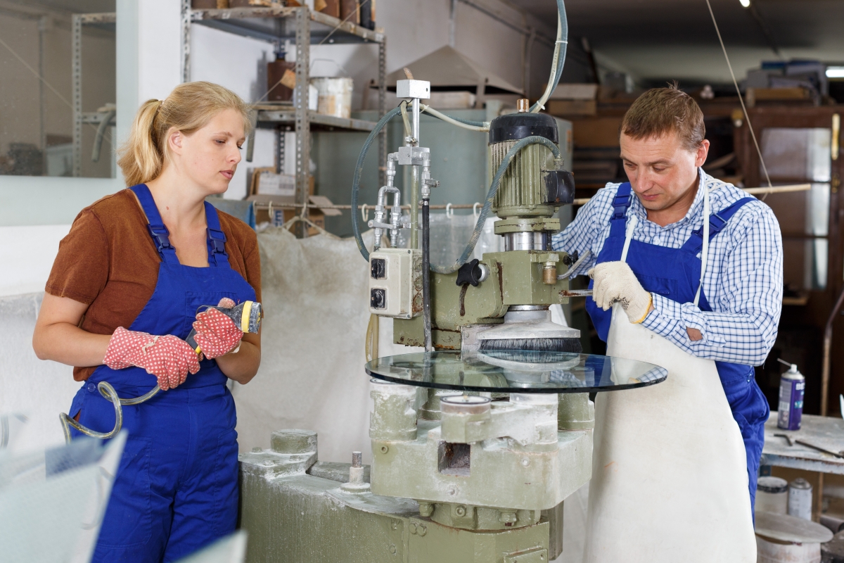 two people, wearing gloves, working on glass products in an industrial setting