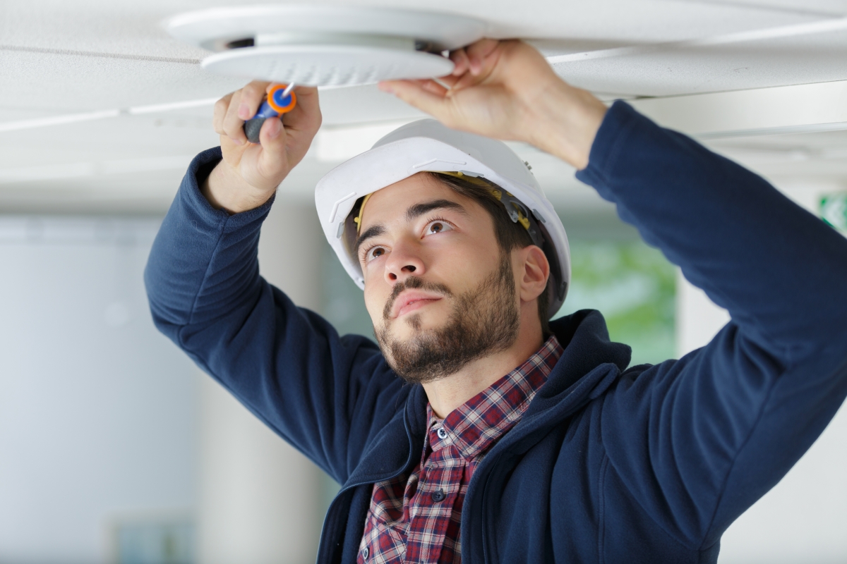 man in hard hat using a tool to install a device in the ceiling