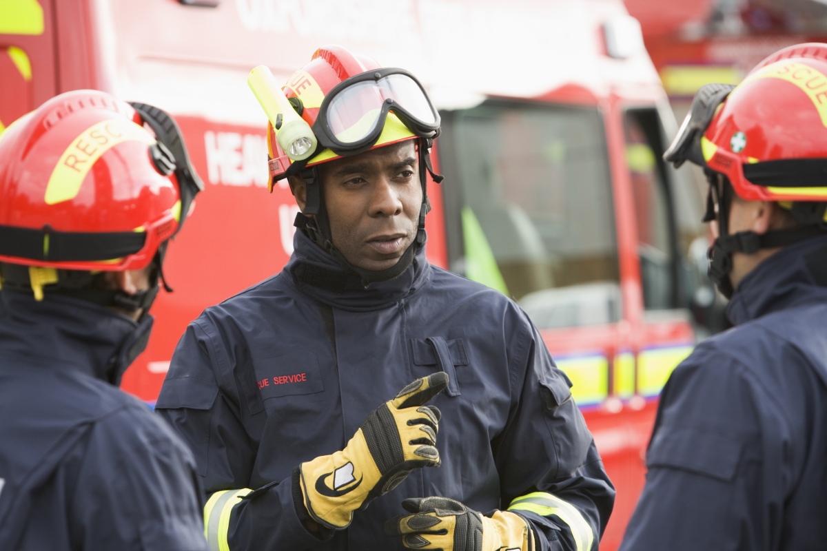 three emergency service workers talking while standing beside emergency service vehicles