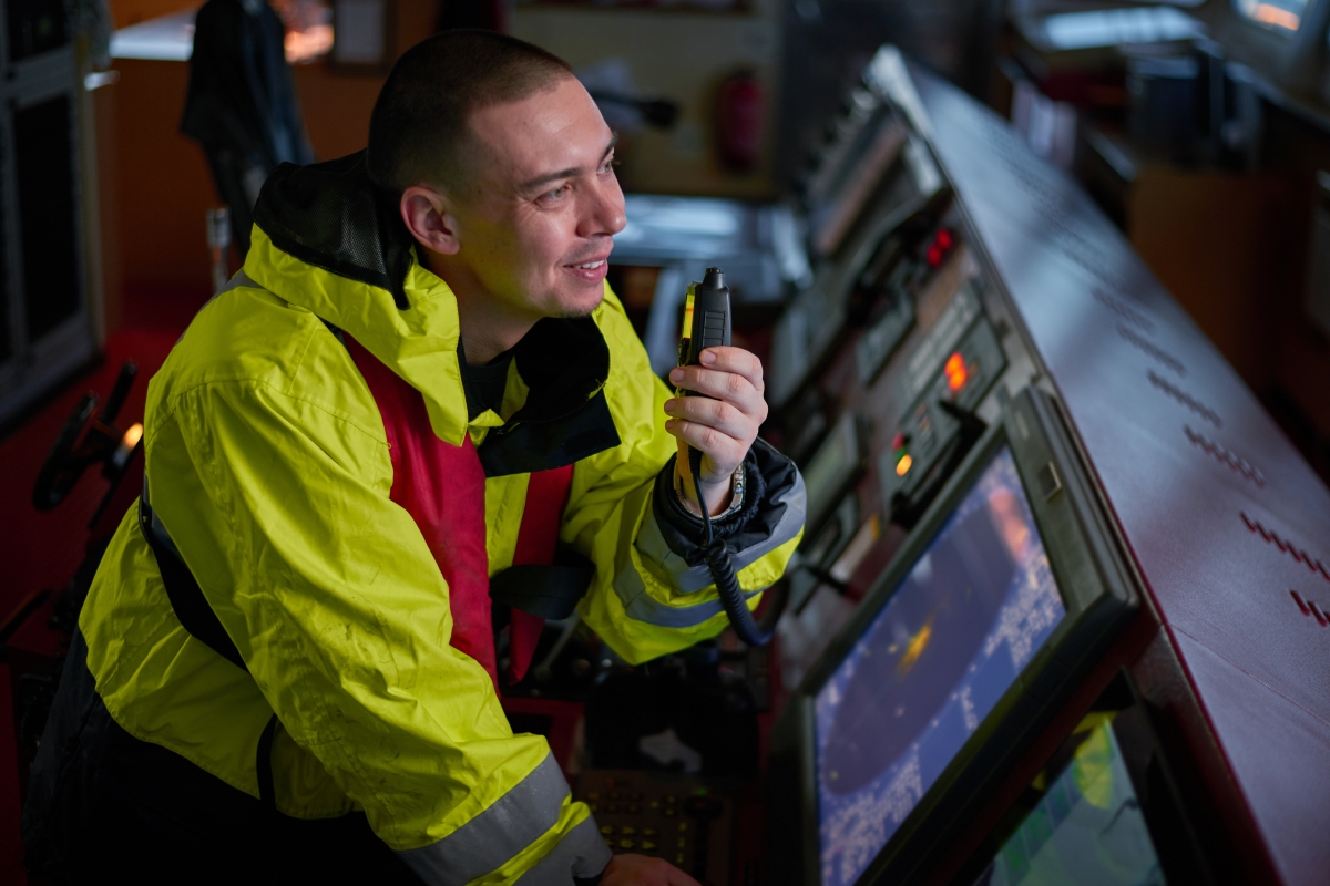 man in safety jacket sitting at a traffic control console speaking into a communications device
