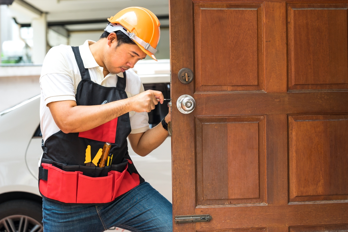 male wearing a toolbelt fixing the lock on an exterior door