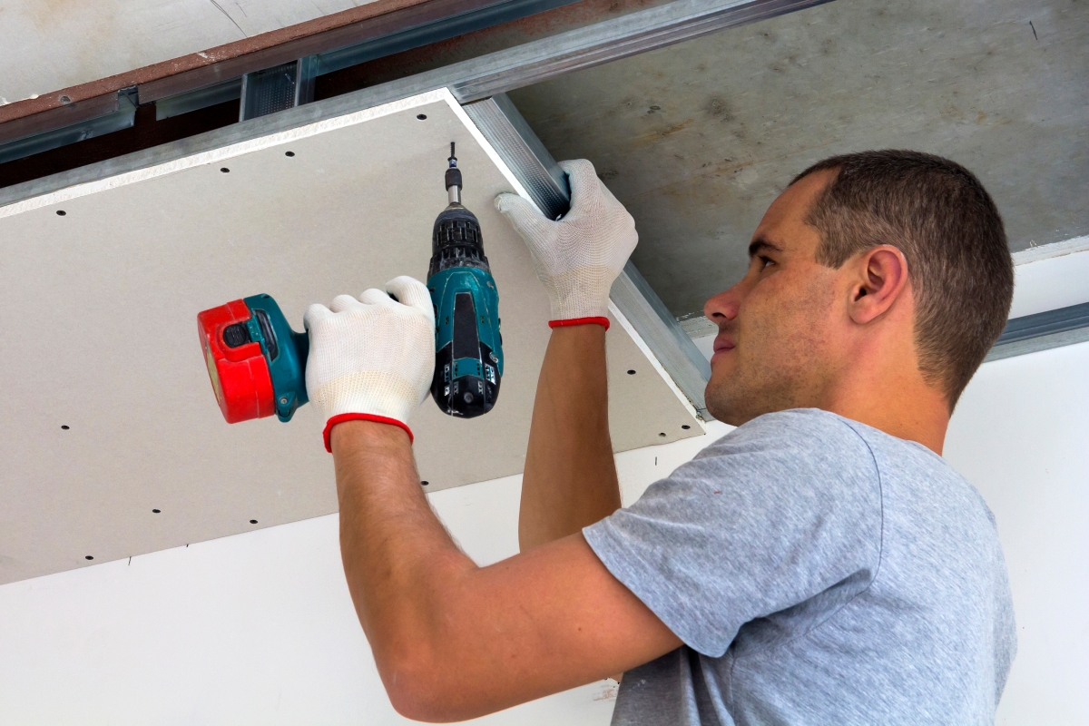 male worker wearing white gloves drilling into the ceiling