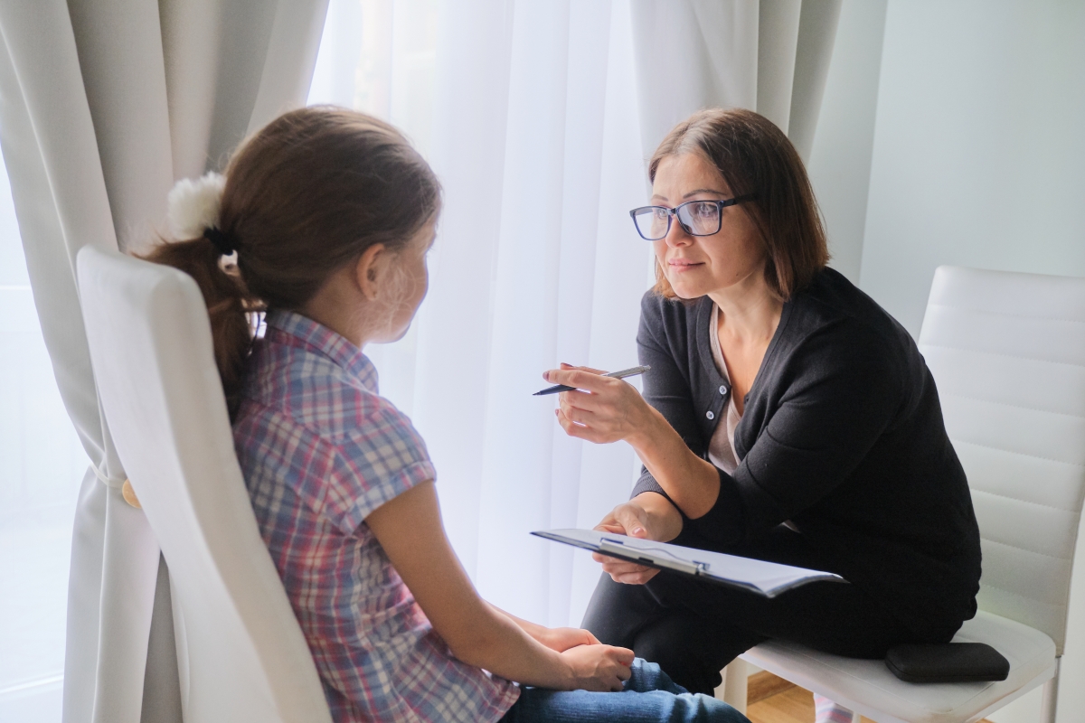 woman sitting across from a young girl while holding a pen and clipboard