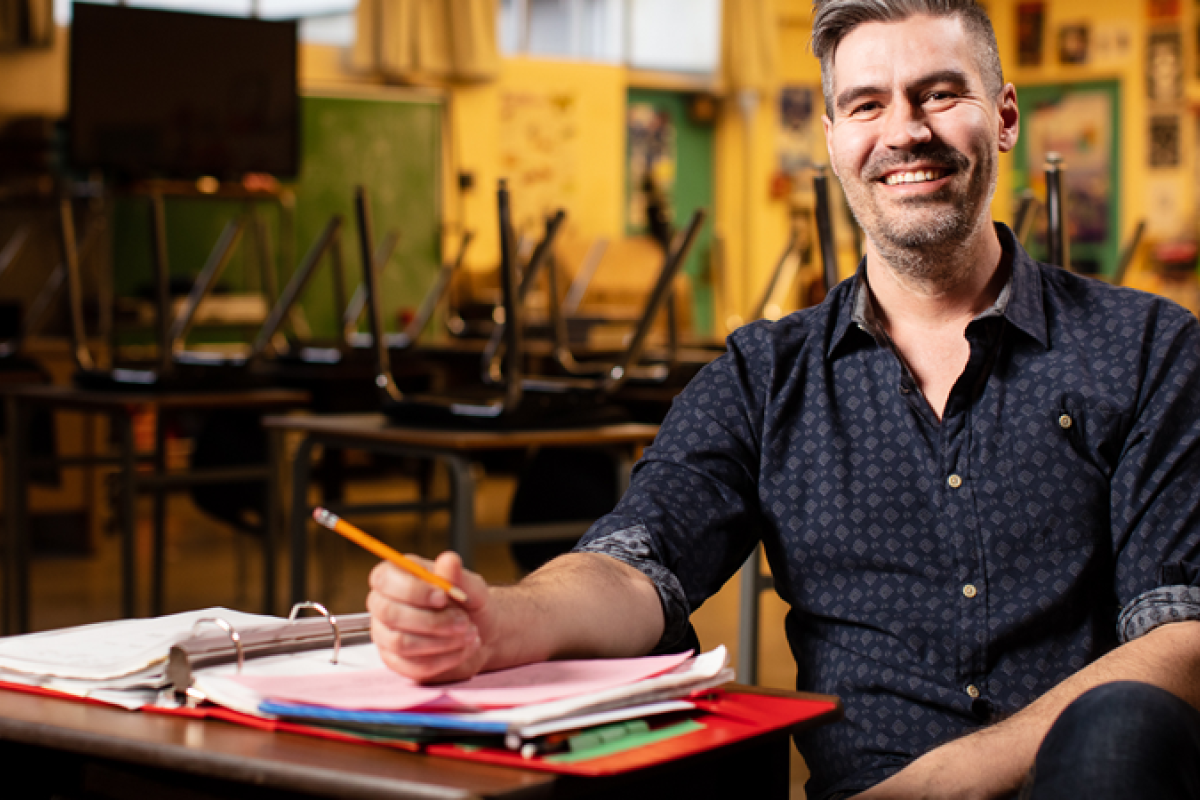 man sitting in an empty classroom, making notes in a binder