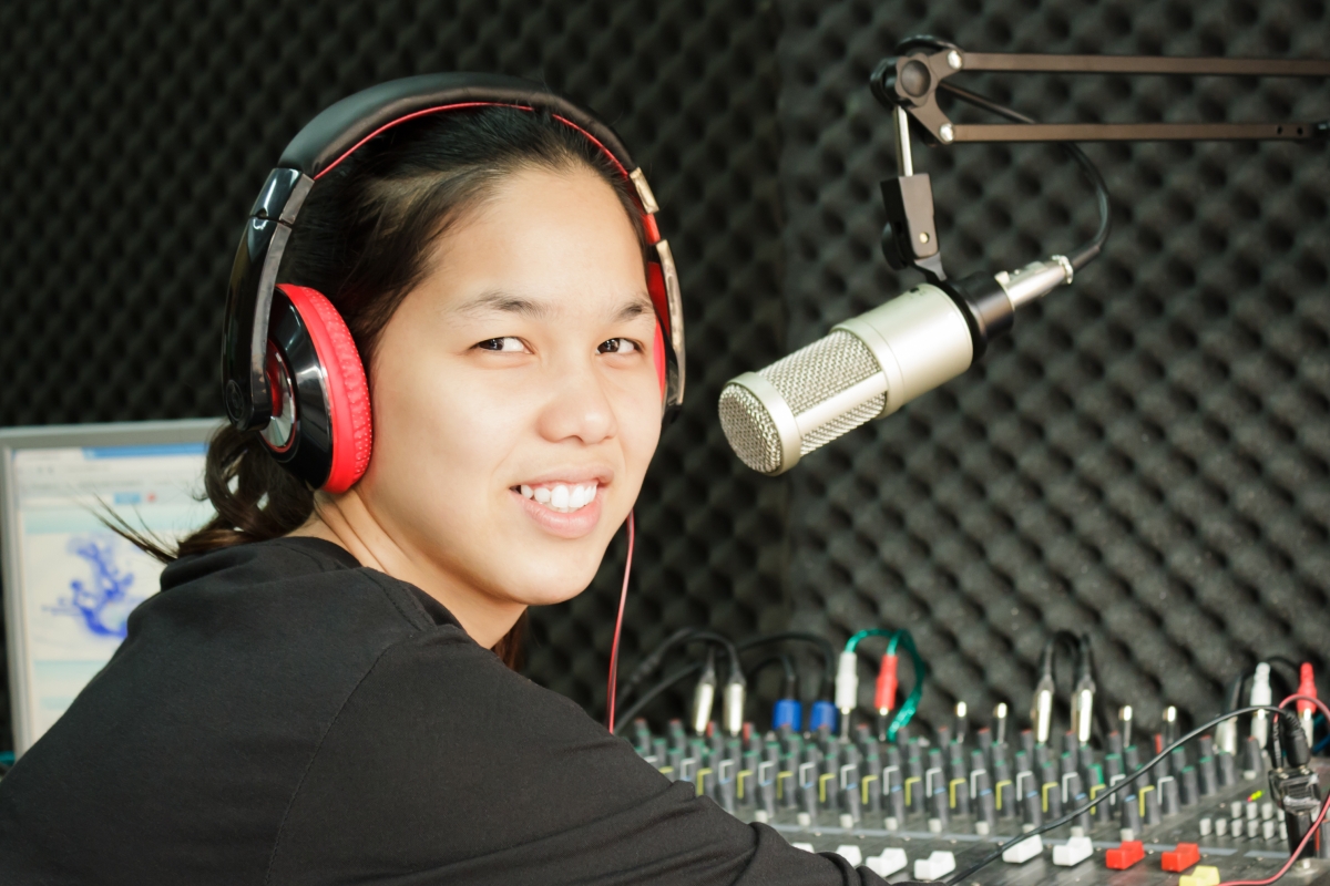 person wearing headphones sitting next to a microphone in a broadcasting station 