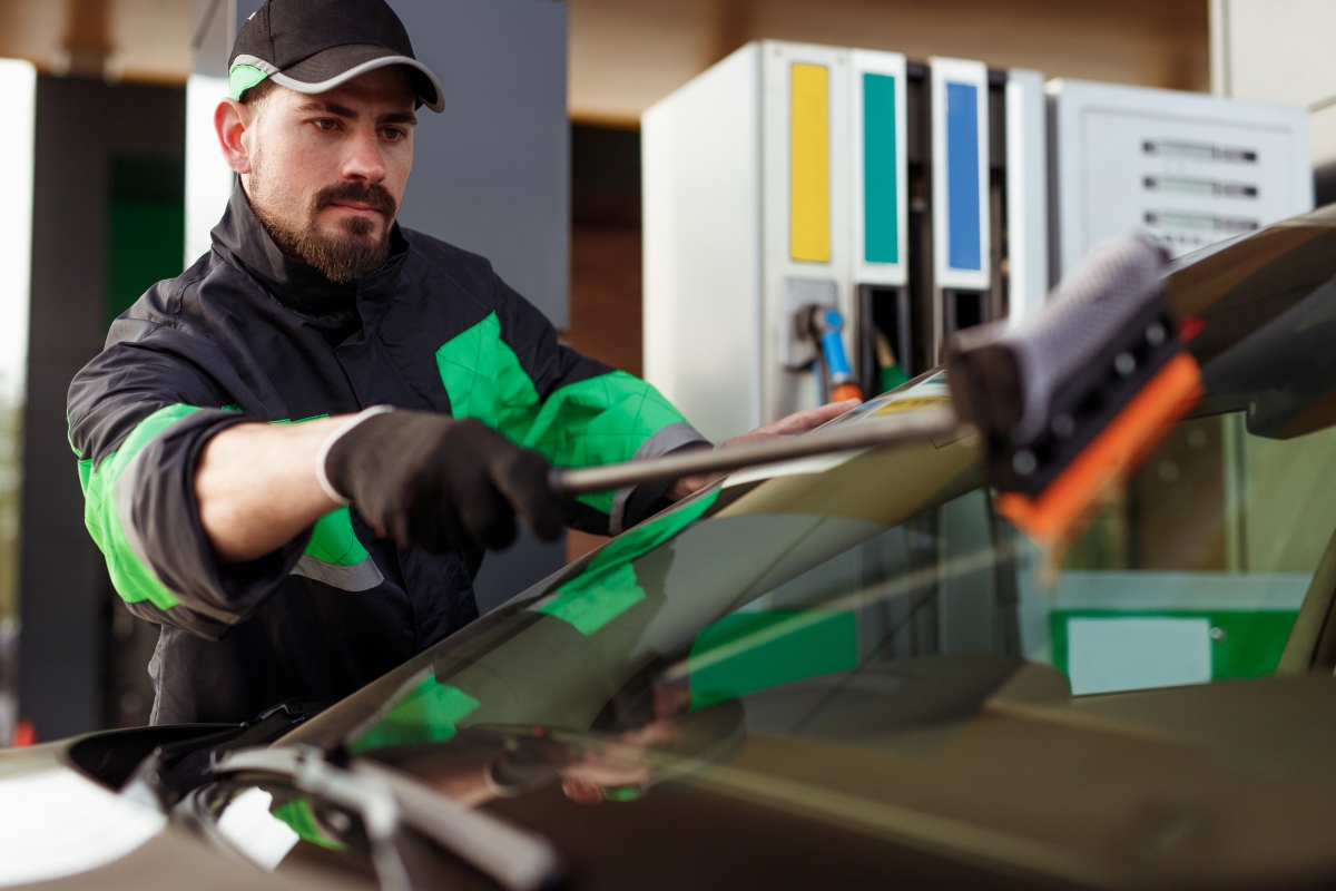 male service station attendant washing the windshield of a vehicle