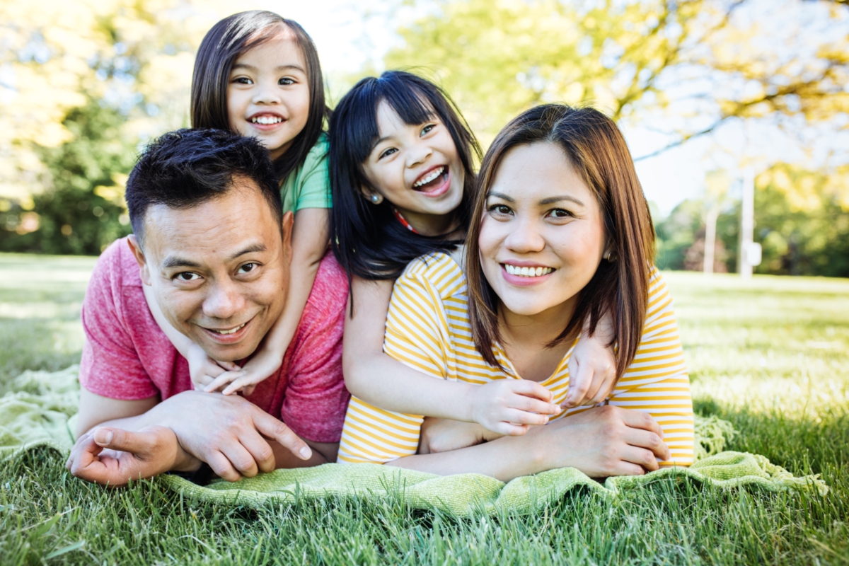 smiling mom and dad with two daughters lying on stomach on grass