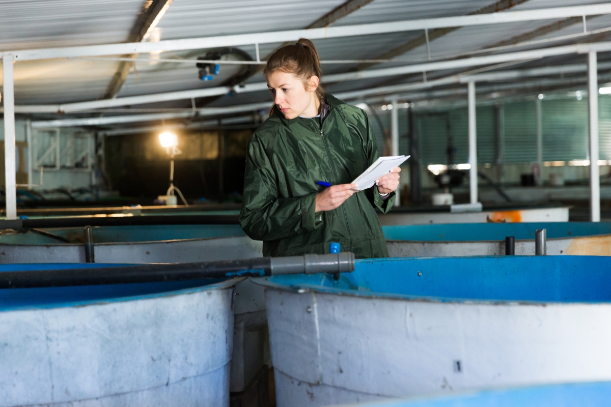 woman holding paper and a pen while surveying large containers
