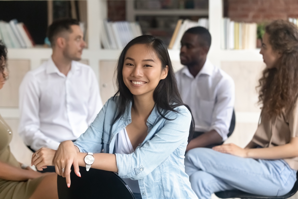 young woman smiling in the foreground with four people sitting in the background talking to each other