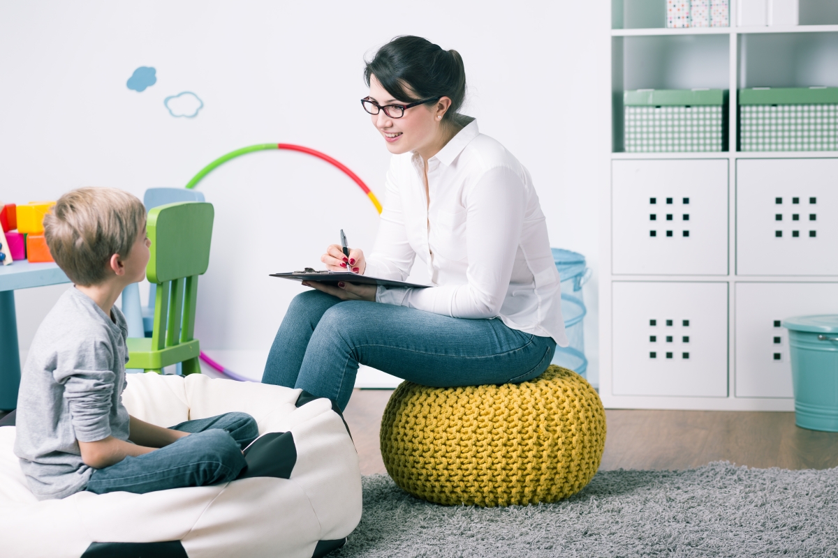 woman sitting across from a child in a playroom, holding a clipboard and pen