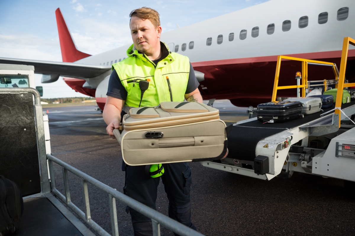 man in reflective vest unloading luggage off a ramp from an airplane onto a trolley