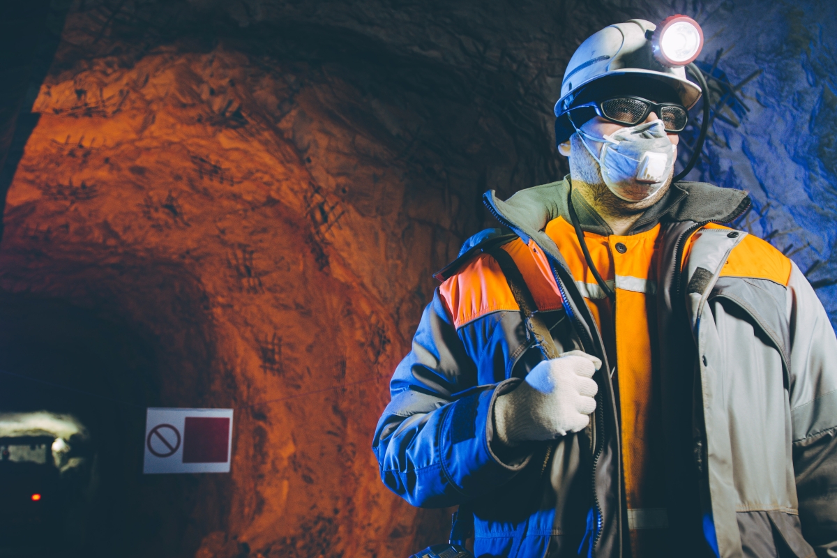 person wearing a hard hat with a light and safety equipment, including a mask, in a mine