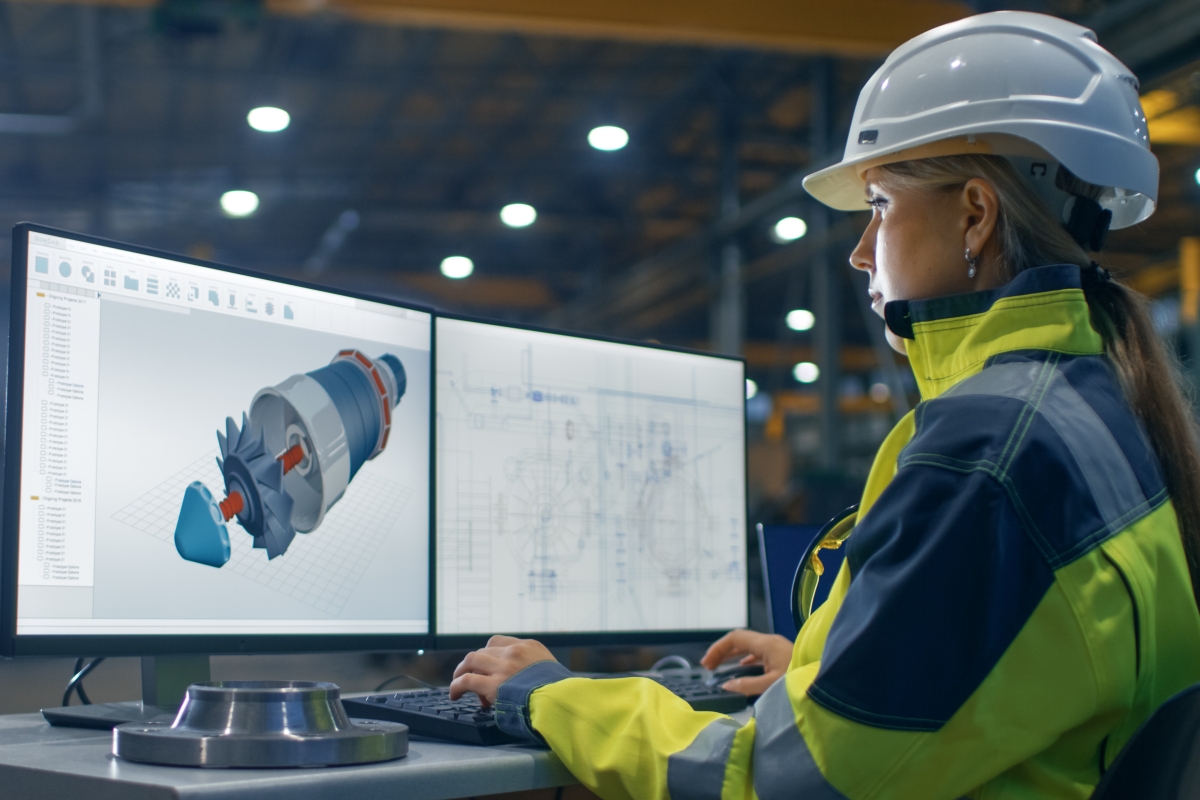 young woman wearing a hard hat and safety vest while looking at a diagram on a computer
