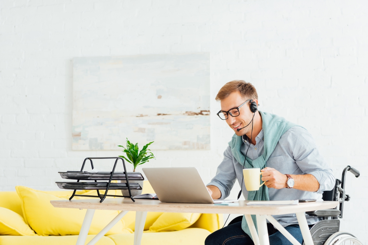 man in wheelchair wearing a headset and sitting at a computer desk working on a laptop