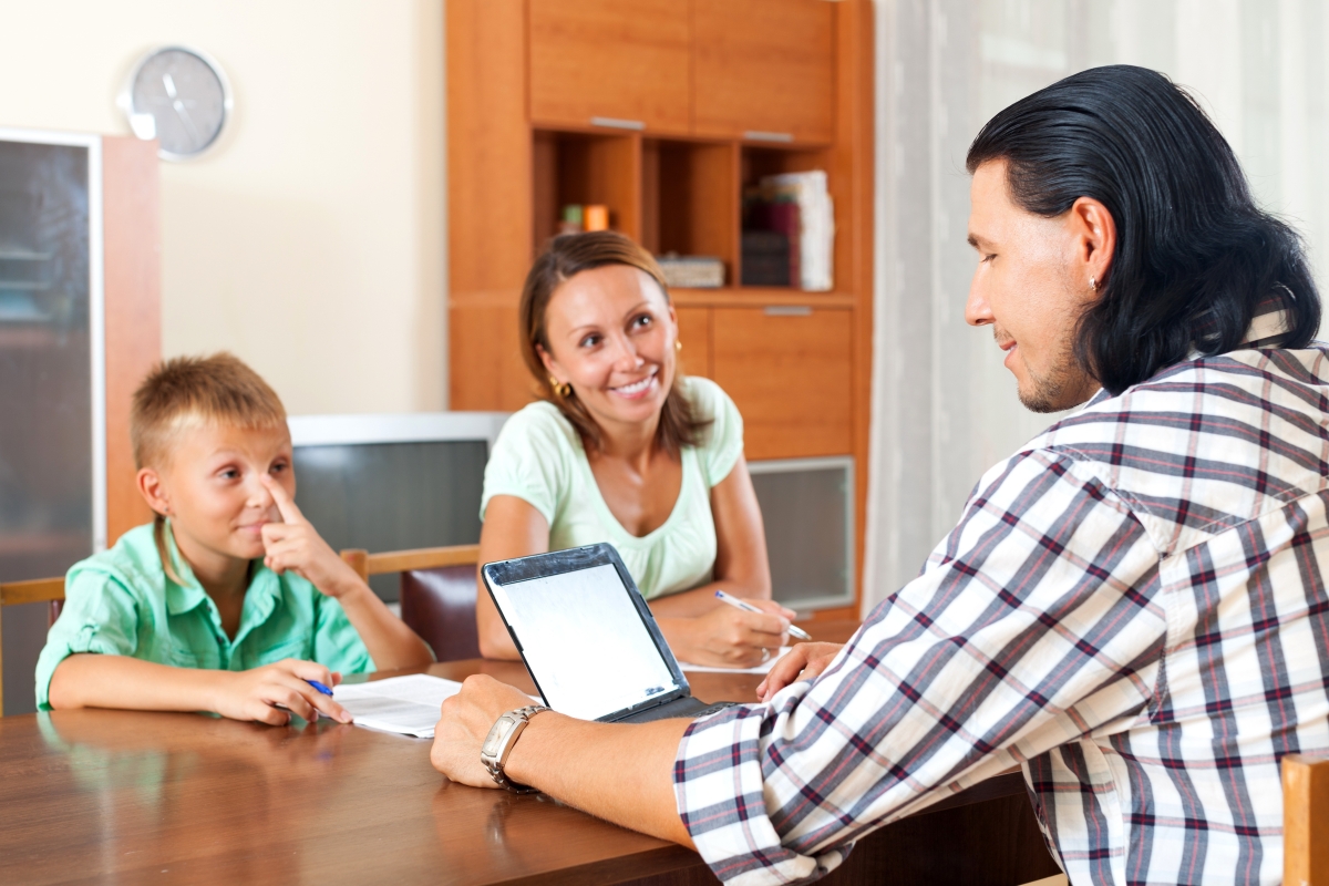man sitting across from a woman and child at a table with a laptop in front of him