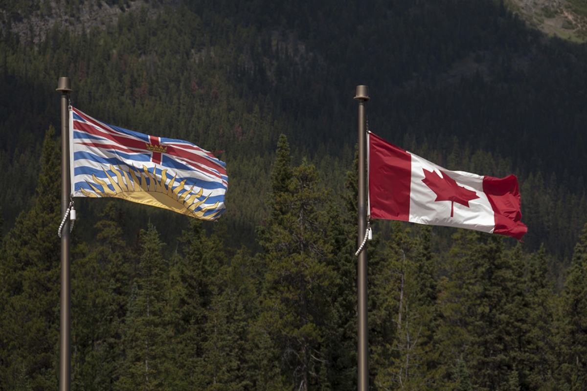 bc and canadian flags flying outside near a forest