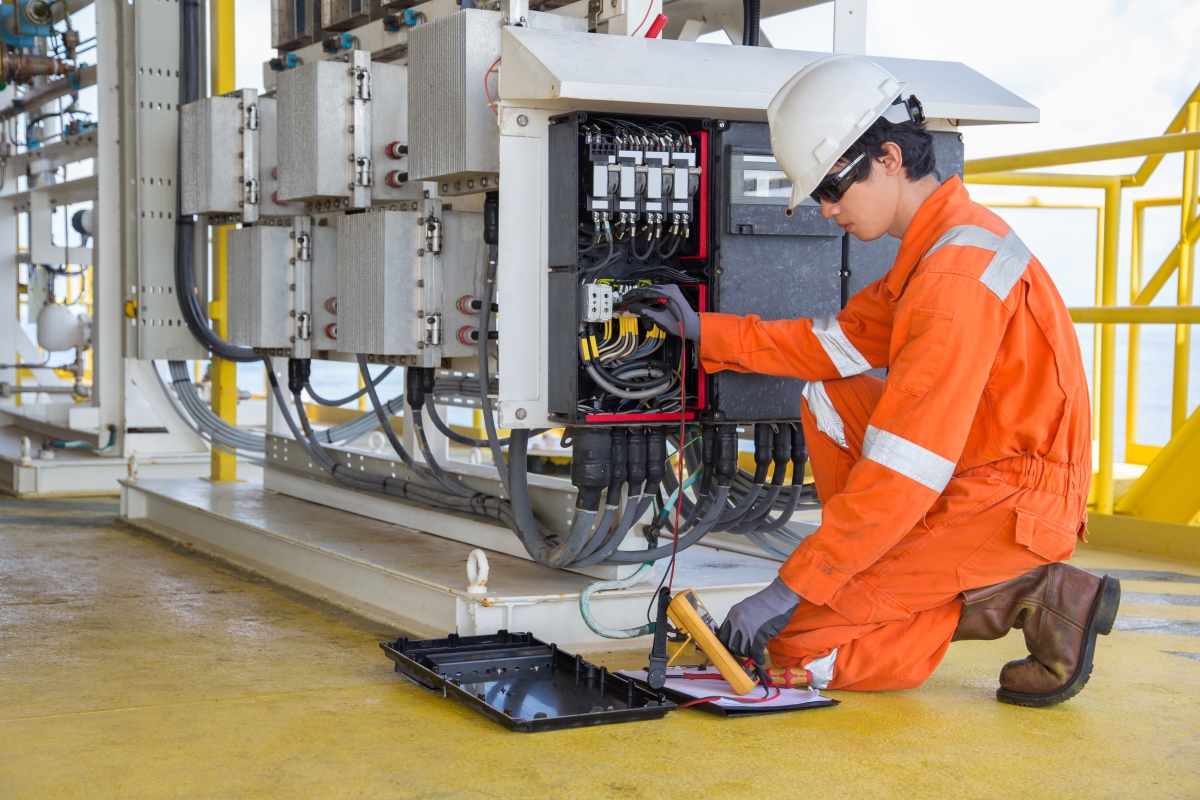 male worker in orange overalls kneeling at a panel of wires