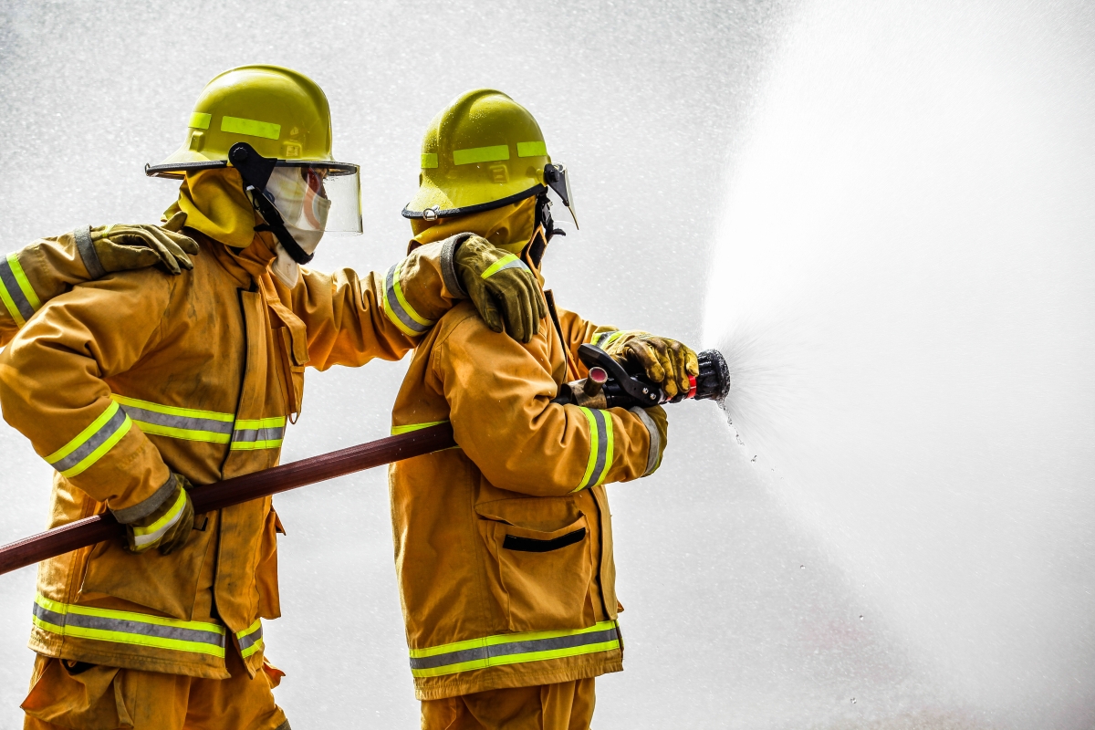two firefighters holding a hose while the one in front sprays and the one behind supports
