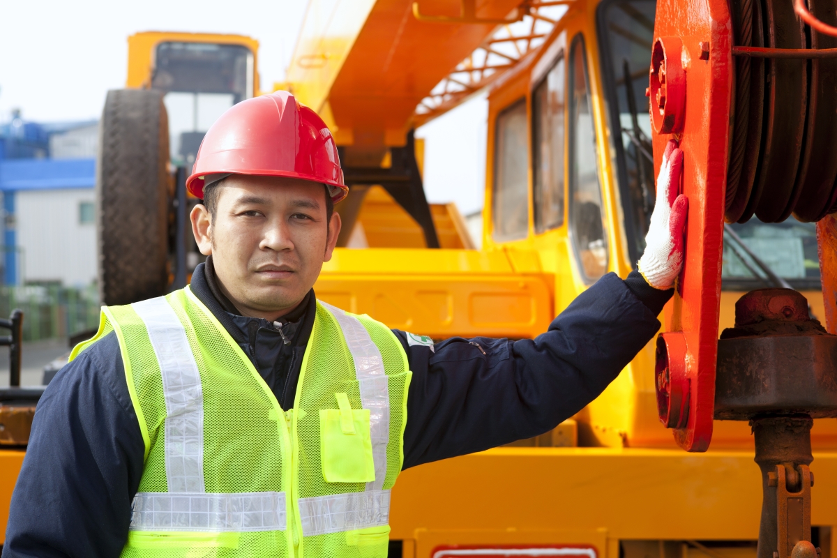 male worker in a hard hat and reflective vest standing near a crane