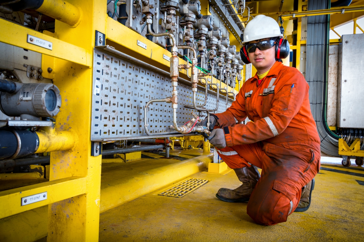man in safety attire kneeling to work on pipes in an industrial setting