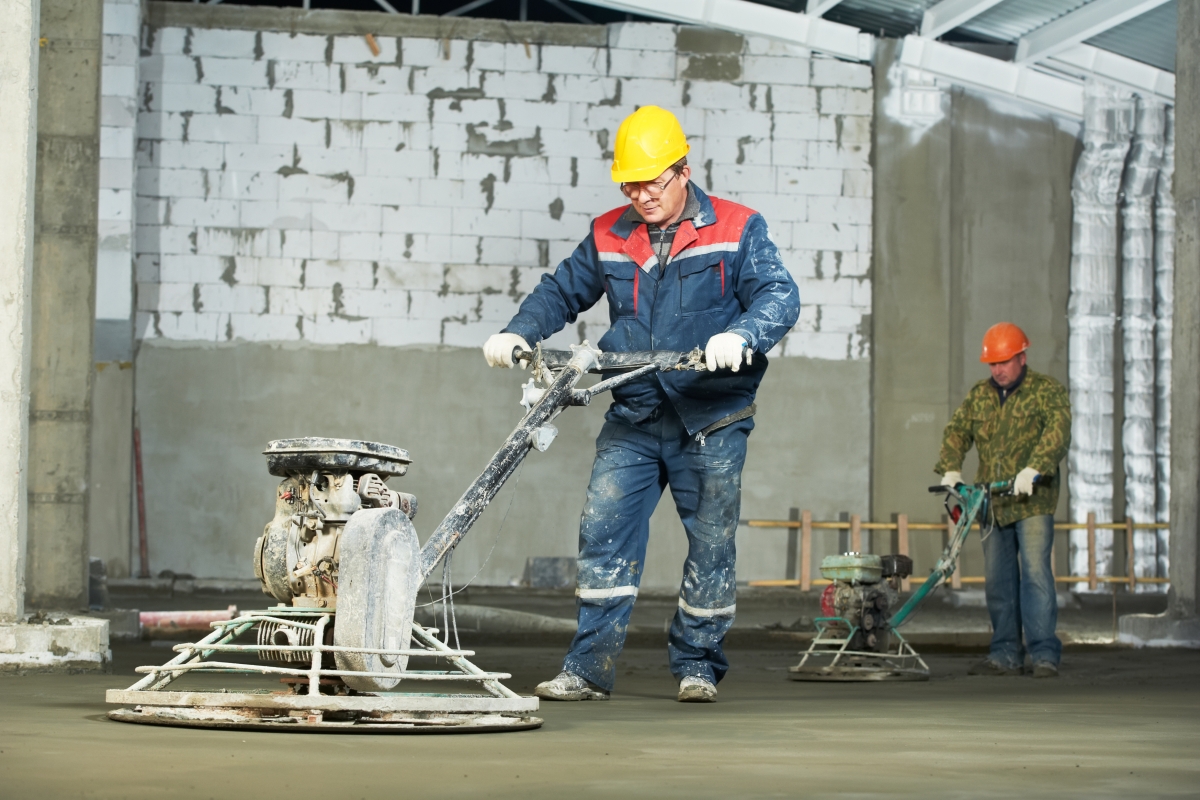 two male workers operating large equipment over concrete floor