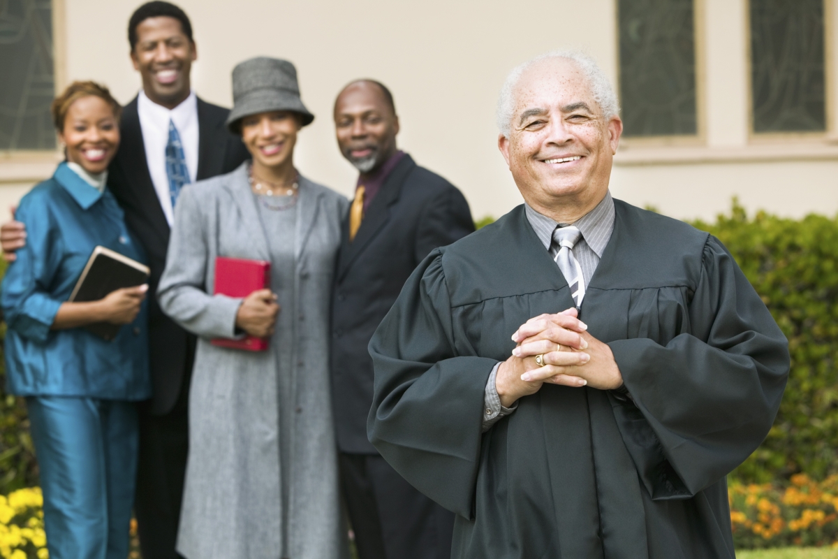 man in religious attire standing in front of a church near a group of dressed up people holding religious books