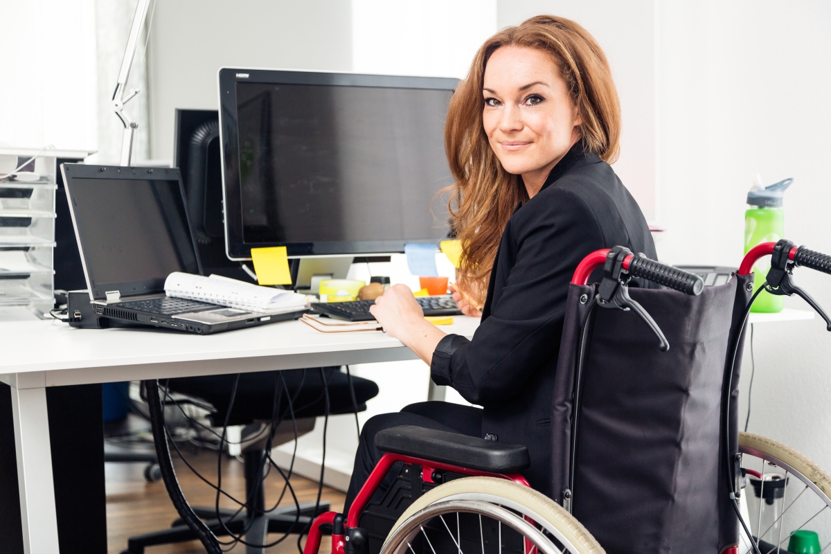 smiling woman sitting in a wheelchair at a computer desk