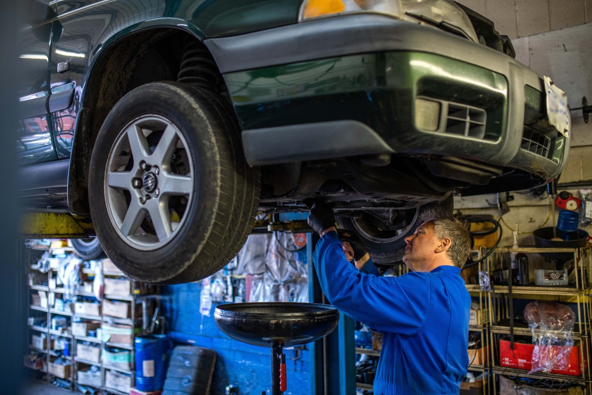 man in overalls repairing a car that is raised on a hoist