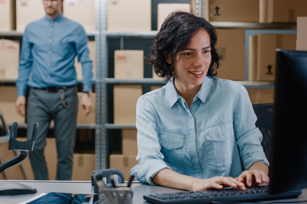 woman typing at a computer while seated at a desk in a warehouse