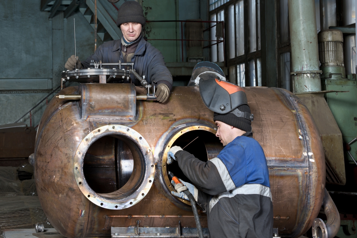 two boilerworkers repairing a large metal boiler