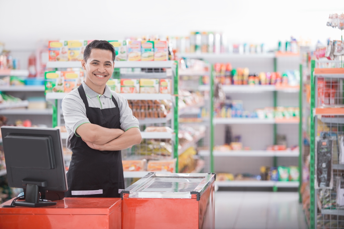 male cashier standing behind a cash register in a grocery store
