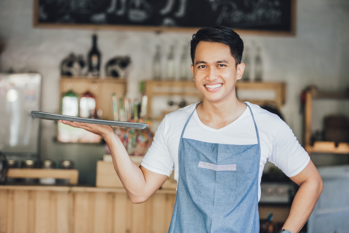 man in apron holding a tray in a café